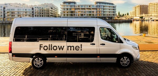 Bild vergr&ouml;&szlig;ern: Ein Kleinbus steht am Hafenbecken. Im Hintergrund sind moderne H�usere zu sehen. Der Bus tr�gt die Aufschrift Follow me!