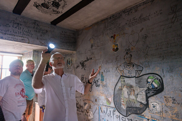 Bild vergr&ouml;&szlig;ern: Historiker f�hrt Besucher durch eine Halle mit historischem Graffiti an den W�nden