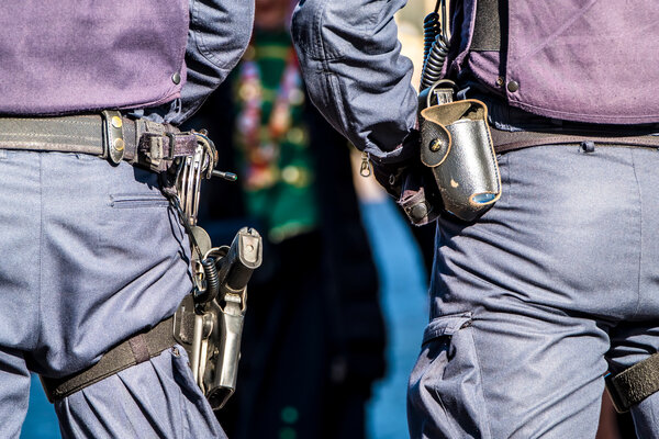 Bild vergr&ouml;&szlig;ern: Nahaufnahme der Dienstg&uuml;rtel von zwei Einsatzkr&auml;ften der Bundespolizei in dunkelblauen Uniformen von hinten. Am G&uuml;rtel der linken Person ist eine Dienstpistole im Beinhohlster zu sehen, rechts eine Ausr&uuml;stungstasche und ein Funkger&auml;t.